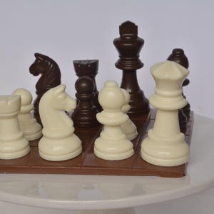 May include: A chocolate chess set with white and brown pieces on a chocolate board. The pieces are arranged in a traditional chess formation.