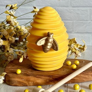 May include: A yellow chocolate honeycomb egg with a gold bee on the side. The egg is on a wooden board with a wooden mallet and yellow candy balls.