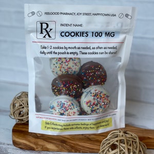 May include: A white resealable bag with a label that reads "FEELGOOD PHARMACY, JOY STREET, HAPPYTOWN USA" and "PATIENT NAME: COOKIES 100 MG". The bag contains chocolate-covered cookies with colorful sprinkles. The label also says "Take 1-2 cookies by mouth as needed, as often as needed, daily until the pouch is empty. These cookies can be shared!"