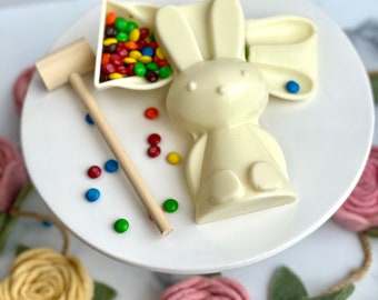 May include: White chocolate bunny candy mold with a separate chocolate bunny ear mold filled with colorful candy. A wooden mallet is included for breaking the chocolate.
