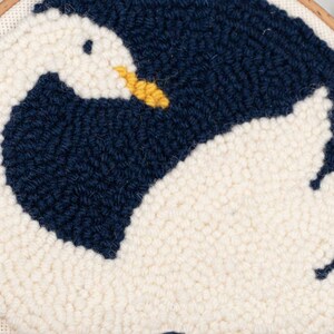 K&ouml;nnte beinhalten: Eine wei&szlig;e und marineblaue Nadelfilz-Stickerei eines Schwans mit gelbem Schnabel. Der Schwan ist zu einem Kreis zusammengerollt, mit dem Kopf unter dem Fl&uuml;gel. Die Stickerei ist in einem Holzrahmen eingefasst.