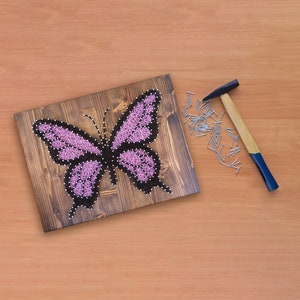 May include: A pink butterfly string art project on a wooden board with a hammer and nails scattered around it.