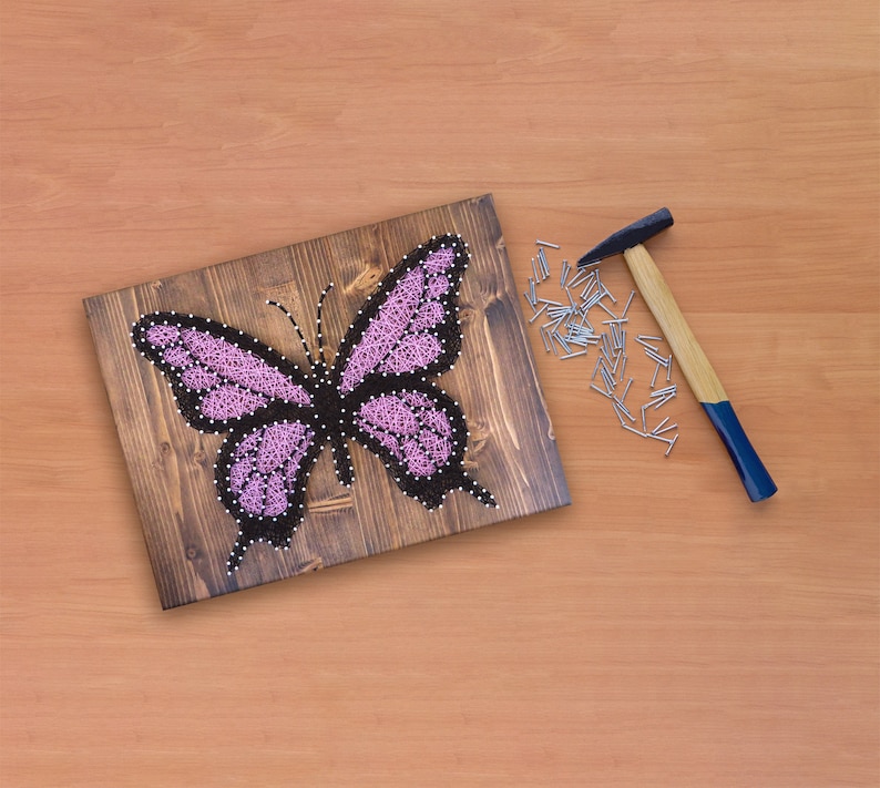 May include: A pink butterfly string art project on a wooden board with a hammer and nails scattered around it.