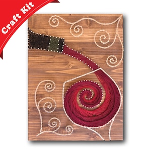 May include: A red and white string art piece depicting a wine bottle pouring wine into a glass. The background is a wooden board with a swirl design.