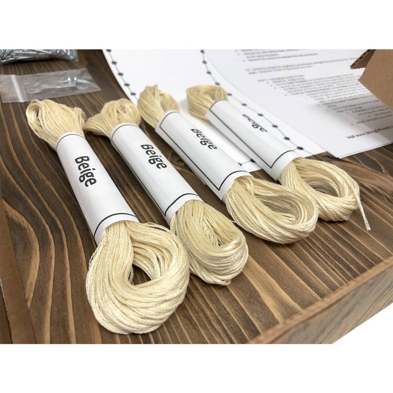 Puede incluir: Cuatro carretes de hilo de bordar beige con la palabra "Beige" impresa en cada carrete.