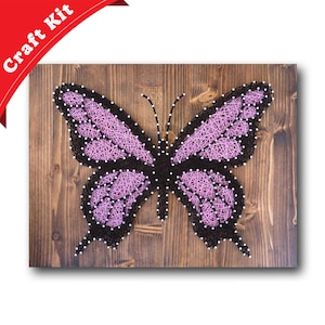 May include: A craft kit featuring a pink and black butterfly string art design on a wooden background. The butterfly is made with string wrapped around nails hammered into the wood.
