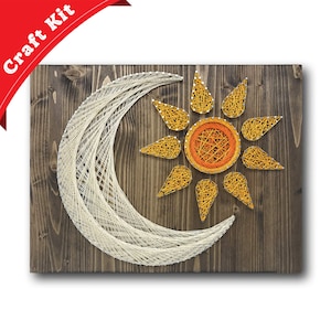 May include: A string art craft kit featuring a white crescent moon and a yellow sun with an orange center on a brown wooden background.