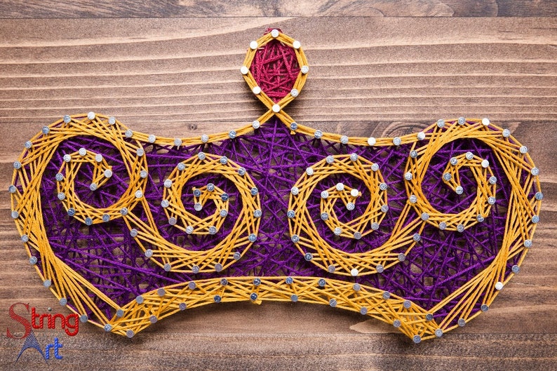 May include: A purple and yellow string art crown with a red jewel on top. The crown is made of string wrapped around nails hammered into a wooden board.