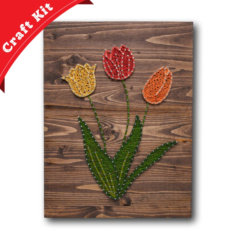 May include: A string art craft kit featuring three tulips with yellow, red, and orange string on a wooden background.