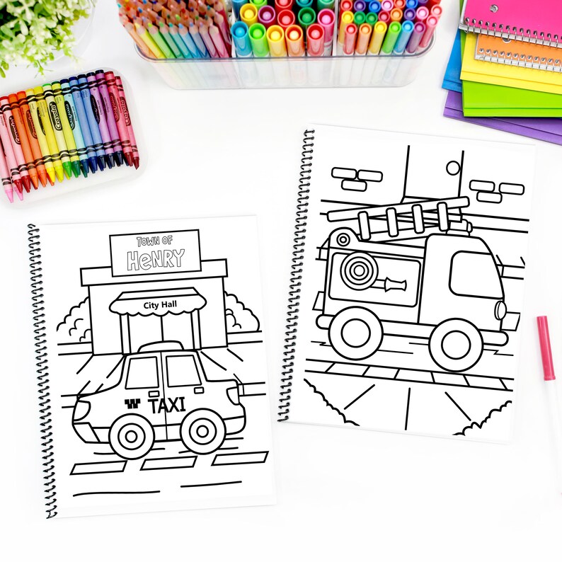 May include: Two spiral-bound colouring books with black and white illustrations. One shows a taxi in front of a city hall with "Town of Henry" and "City Hall" text. The other depicts a fire engine. Crayons and markers are visible.