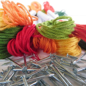 May include: A close-up of a pile of colorful embroidery floss spools and a pile of silver nails. The floss is in shades of green, orange, red, and yellow.
