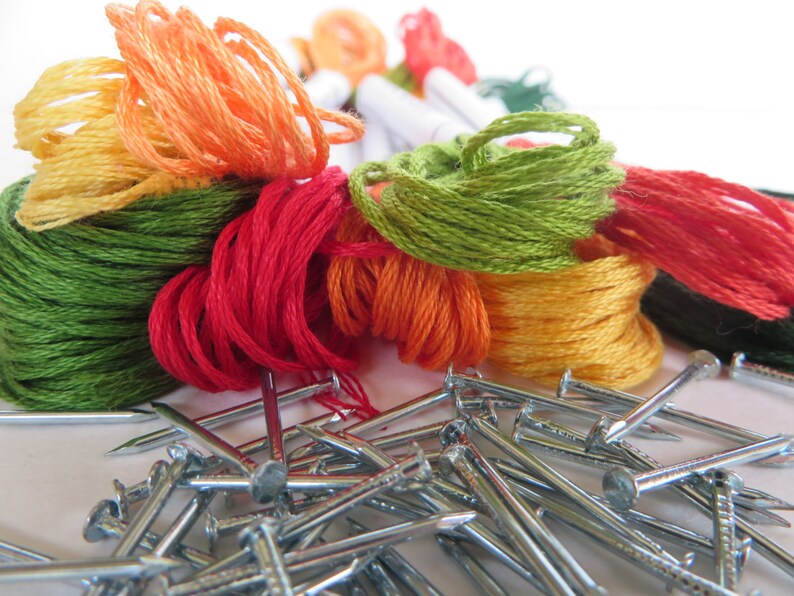 May include: A close-up of a pile of colorful embroidery floss spools and a pile of silver nails. The floss is in shades of green, orange, red, and yellow.