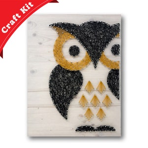 May include: A string art craft kit featuring an owl design. The owl is made with black and gold string wrapped around nails hammered into a wooden board.