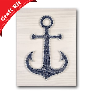 May include: A navy blue string art anchor on a white wooden background. The anchor is made of string wrapped around nails hammered into the wood.