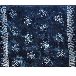 May include: A dark blue sarong with a white floral pattern. The sarong has a fringe border and white decorative edges. The fabric has a mottled appearance, and the floral design is evenly spaced across the surface.
