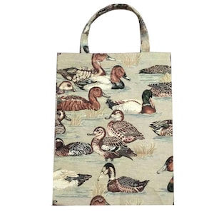 May include: A rectangular tote bag featuring a woven tapestry pattern of multiple ducks swimming in water. The ducks are depicted in shades of brown, white, green, and black against a light beige background. The bag has a single top handle.