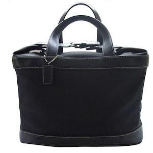 May include: A black canvas tote bag with leather trim and a top handle. The bag has a buckle closure and a small silver charm.