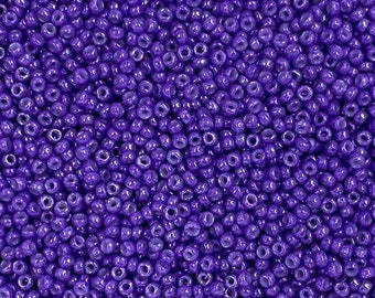 May include: A close-up shot of a large pile of small, round, purple seed beads. The beads are densely packed together, filling the frame. The color is a deep, vibrant purple, and the beads appear to have a glossy finish. Ideal for jewelry making and crafts.