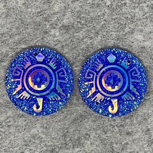 May include: Two blue iridescent glitter round resin earrings with a geometric design in the center.