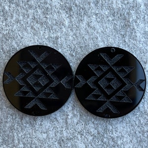 May include: Two black round wooden coasters with a geometric design. The design is a repeating pattern of triangles and squares.
