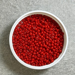 May include: A white bowl filled with bright red seed beads.