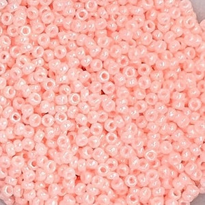 Puede incluir: Vista de cerca de una gran cantidad de pequeñas cuentas redondas de color rosa claro. Las cuentas tienen un acabado ligeramente iridiscente.