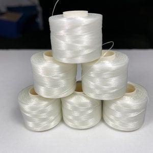 May include: A stack of six spools of white thread. The thread is tightly wound around a cylindrical core. The spools are arranged in a pyramid shape, with one spool at the top, two in the middle, and three at the bottom.