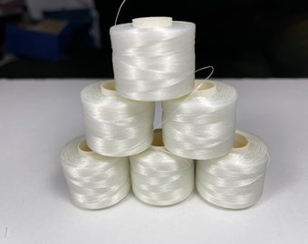 May include: A stack of six spools of white thread. The thread is tightly wound around a cylindrical core. The spools are arranged in a pyramid shape, with one spool at the top, two in the middle, and three at the bottom.