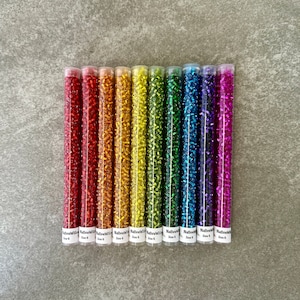 May include: Ten tubes of iridescent glass seed beads in a rainbow of colours, including red, orange, yellow, green, blue, indigo, and violet. Each tube is labelled "NativeWilo Size 6".