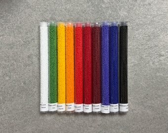 May include: A collection of ten clear tubes filled with small, colorful beads. The tubes display a spectrum of colors, including white, green, yellow, orange, red, burgundy, purple, blue, and black. Each tube has a white label with text.