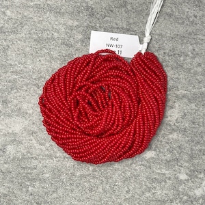 May include: A close-up of a large spool of bright red seed beads. The label reads "Red NW-107 11".