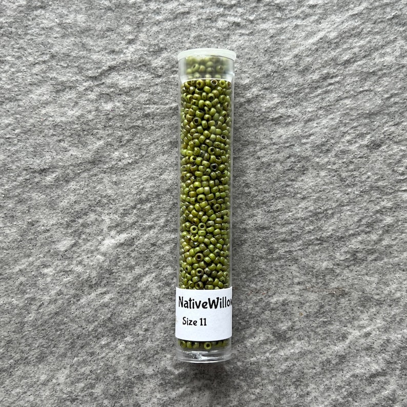 May include: A clear glass tube filled with small, green glass beads. The tube has a white label that reads "NativeWillow Size 11".