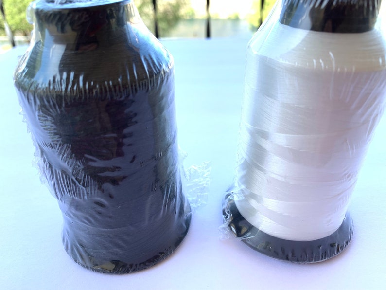 Puede incluir: Dos carretes de hilo, uno negro y uno blanco, envueltos en pl&aacute;stico transparente.