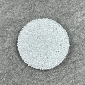 May include: A close-up of a white round container filled with small white beads.