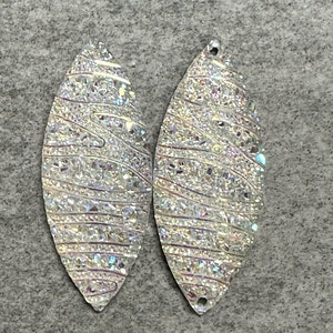 May include: Two silver leaf-shaped earrings with a sparkly, iridescent finish. The earrings have a hole at the top for hanging.