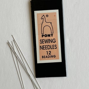 May include: A package of Pony sewing needles for beading, with the brand name and a horse logo. The package is black with a peach-colored label. Several silver needles are scattered beside the package on a white surface.