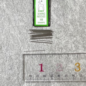 May include: A pack of 10 Pony sewing needles, size 10 sharps, with a green and white label featuring a horse logo. The needles are arranged in a pile on a gray surface next to a ruler.