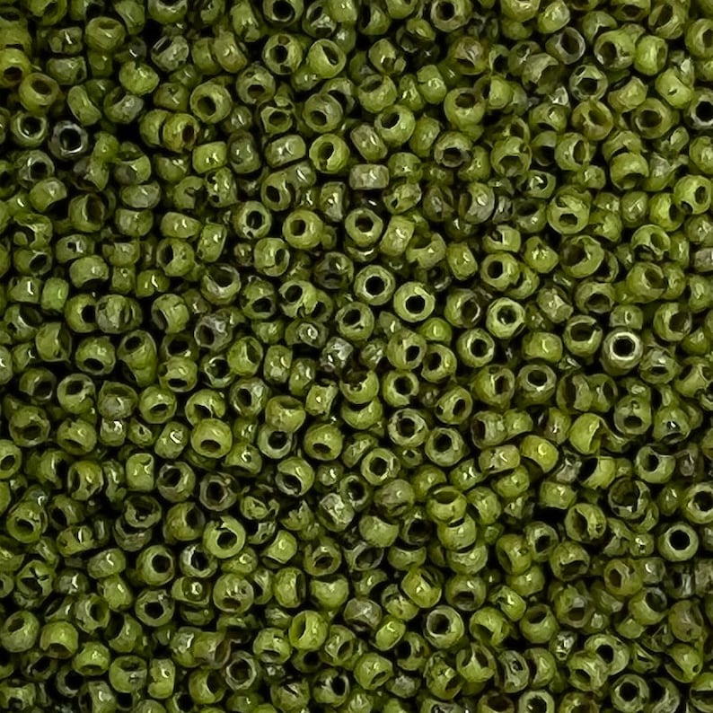 May include: A close-up image of a large quantity of small, round, green glass beads. The beads are opaque and have a slightly irregular shape.