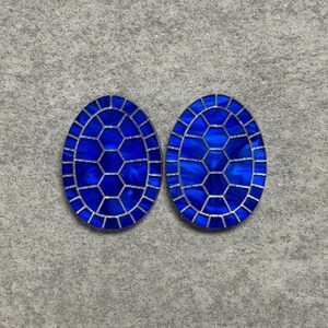 May include: Two oval-shaped, cobalt blue decorative pieces with a silver border. The interior design features a honeycomb pattern. The pieces are displayed on a grey, textured surface.