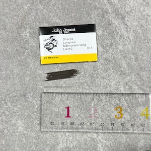 May include: A package of 25 John James Sharps Longues sewing needles, labeled "L4310 011". The needles are arranged in a pile and measure approximately 1 inch in length.
