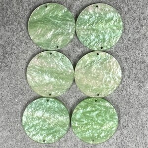 May include: Six round, green, iridescent, resin, embellishments with two holes each. The embellishments have a marbled, swirled pattern.