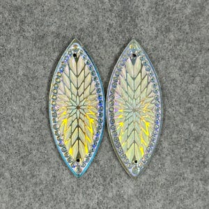 May include: Two iridescent white and blue leaf-shaped embellishments with a geometric pattern. The embellishments have a white center with a blue border.