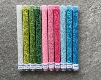 May include: Eleven glass tubes filled with tiny beads in various colours, including white, green, pink, and blue. Each tube is labelled with "NativeWild" and "Size 11". These beads are suitable for crafting projects.