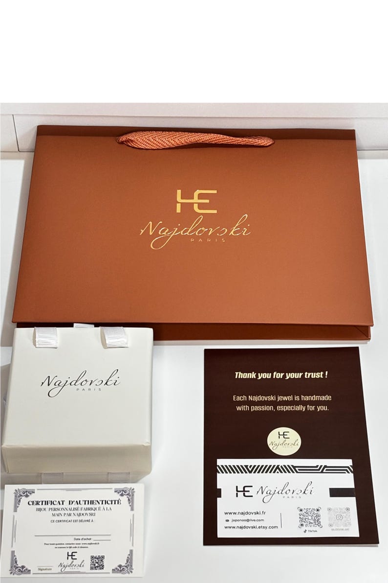 Emballage bijou Najdovski avec sac cadeau marron élégant à logo doré, boîte à bijoux beige et carte de remerciement. Présentation soignée et raffinée, style luxe, idéale pour offrir, esthétique boutique parisienne.