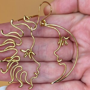 Détails rapprochés des boucles d’oreilles en forme de soleil et de lune, confectionnées à la main en fil doré. Design élégant et minimaliste inspiré du cosmos.