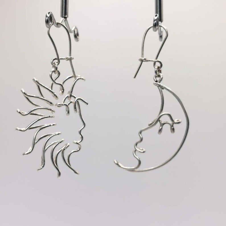 Boucles d’oreilles pendantes avec un design solaire et lunaire, faites à la main en fil métallique doré. Un bijou intemporel aux lignes épurées et artistiques.