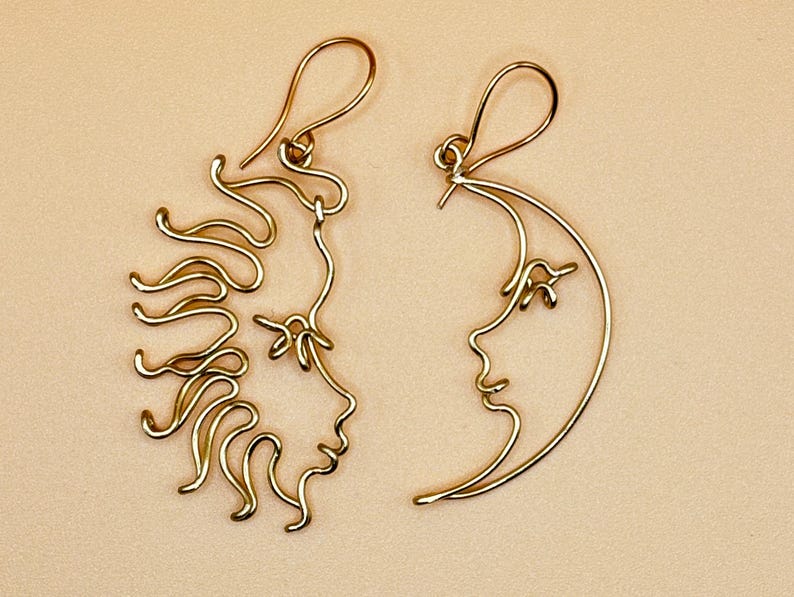Gros plan sur les boucles d’oreilles Soleil et Lune en acier inoxydable doré, mettant en valeur les détails fins du fil torsadé et la finesse du travail artisanal.