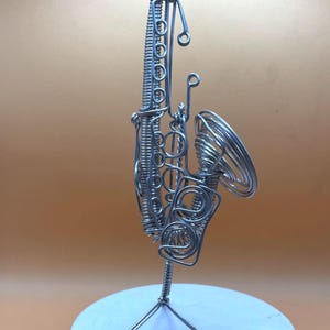 Sculpture moderne de saxophone, faite main en aluminium, avec lumière douce sur fond neutre.