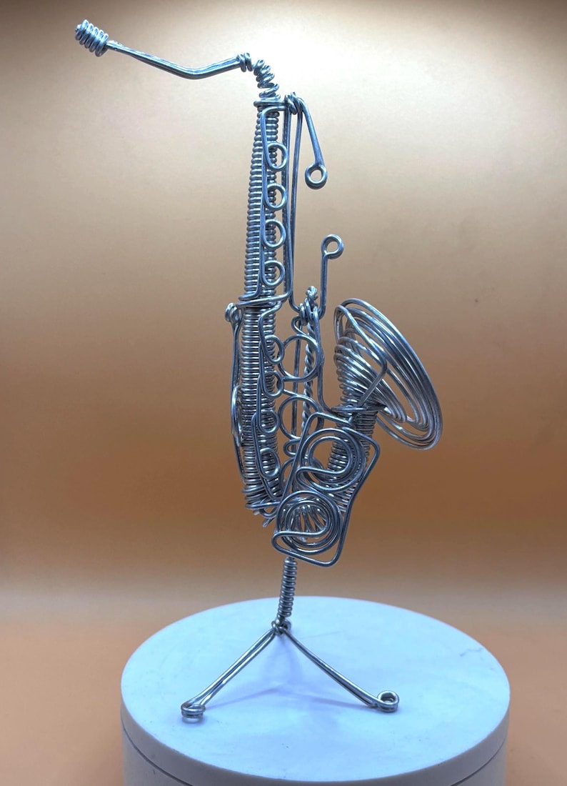 Sculpture moderne de saxophone, faite main en aluminium, avec lumière douce sur fond neutre.