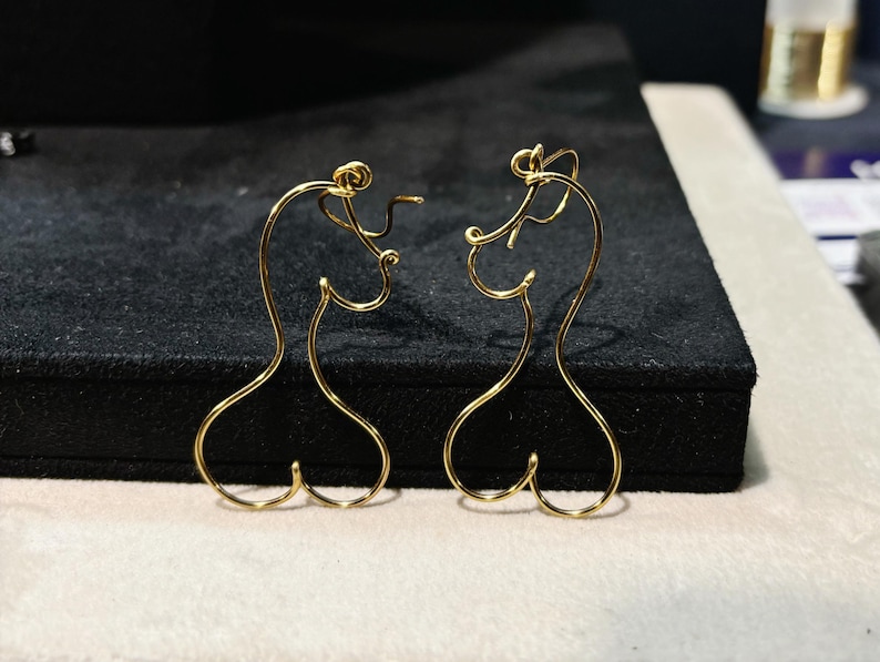 Bijou fait main en fil métallique, formant une silhouette féminine minimaliste avec des courbes élégantes.